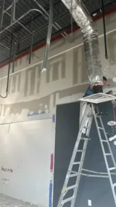 Commercial interior renovation with worker on ladder adjusting duct installation.