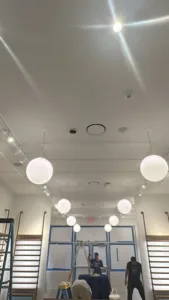 Commercial interior renovation showing workers finishing ceiling lighting fixtures.
