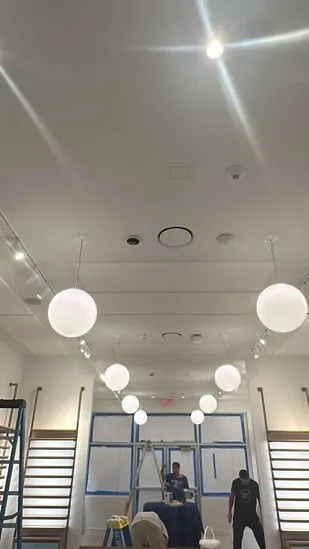 Commercial interior renovation showing workers finishing ceiling lighting fixtures.